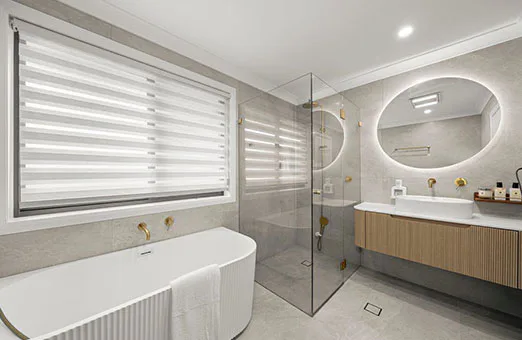 Luxury bathroom with freestanding bathtub, glass shower enclosure, floating vanity with marble top, round backlit mirror, and gold fixtures