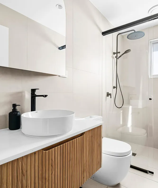 Modern bathroom makeover featuring a fluted timber vanity with white countertop, round vessel basin, matte black tapware, walk-in shower with rain head and glass screen, and neutral beige wall tiles.