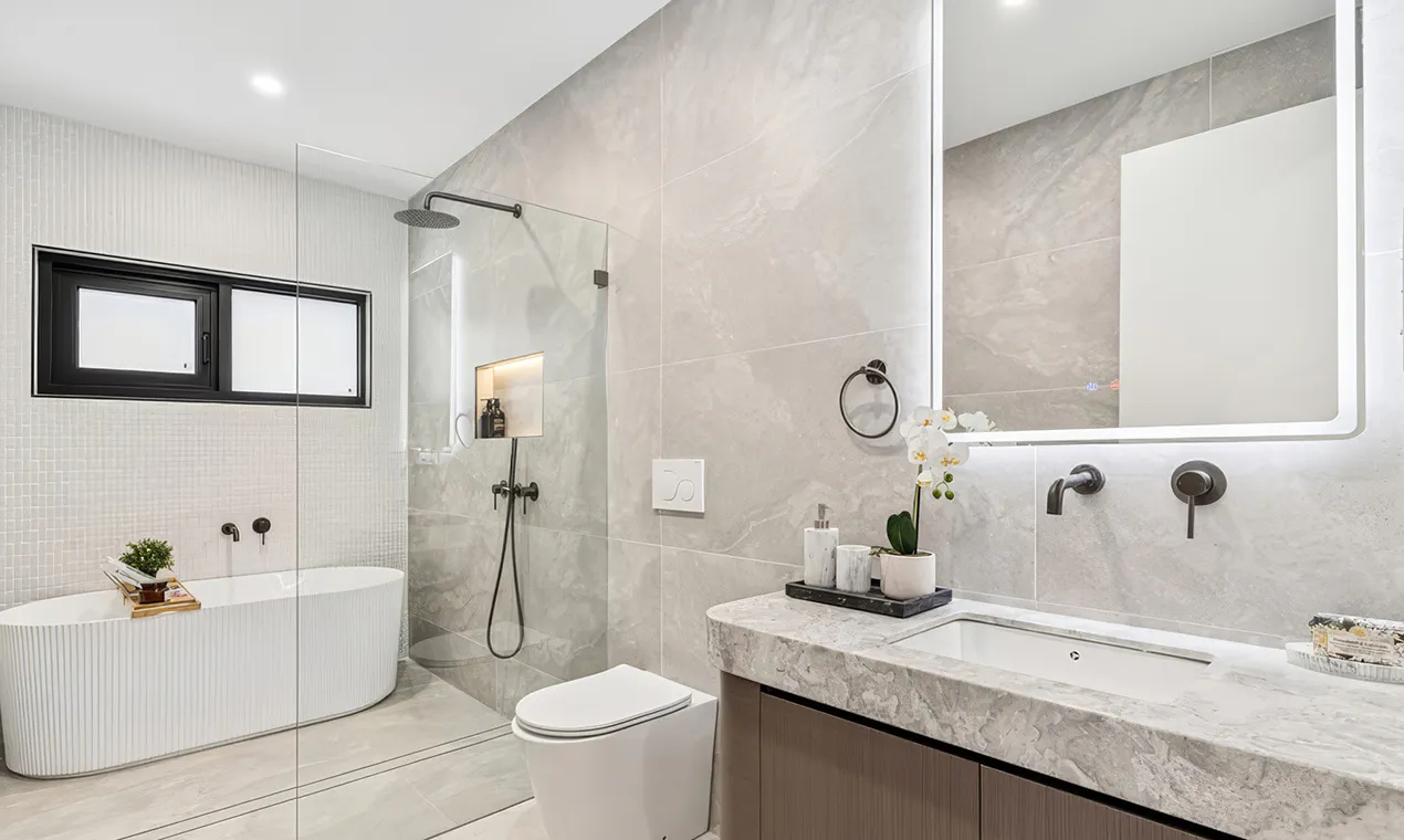 Modern bathroom renovation featuring a freestanding bathtub, walk-in shower with rainfall showerhead, wall-mounted vanity with stone benchtop, and backlit mirror — neutral tones and contemporary fittings creating a sleek, spa-like finish.